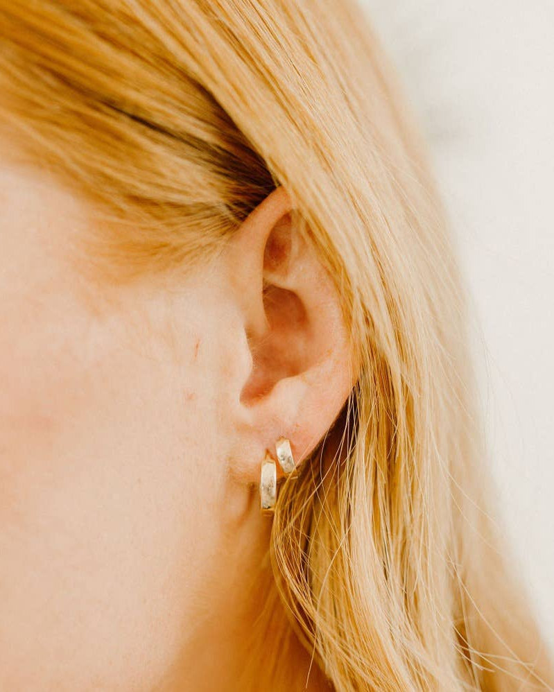 Solid 10k gold large huggie hoop earrings worn on a woman's ear