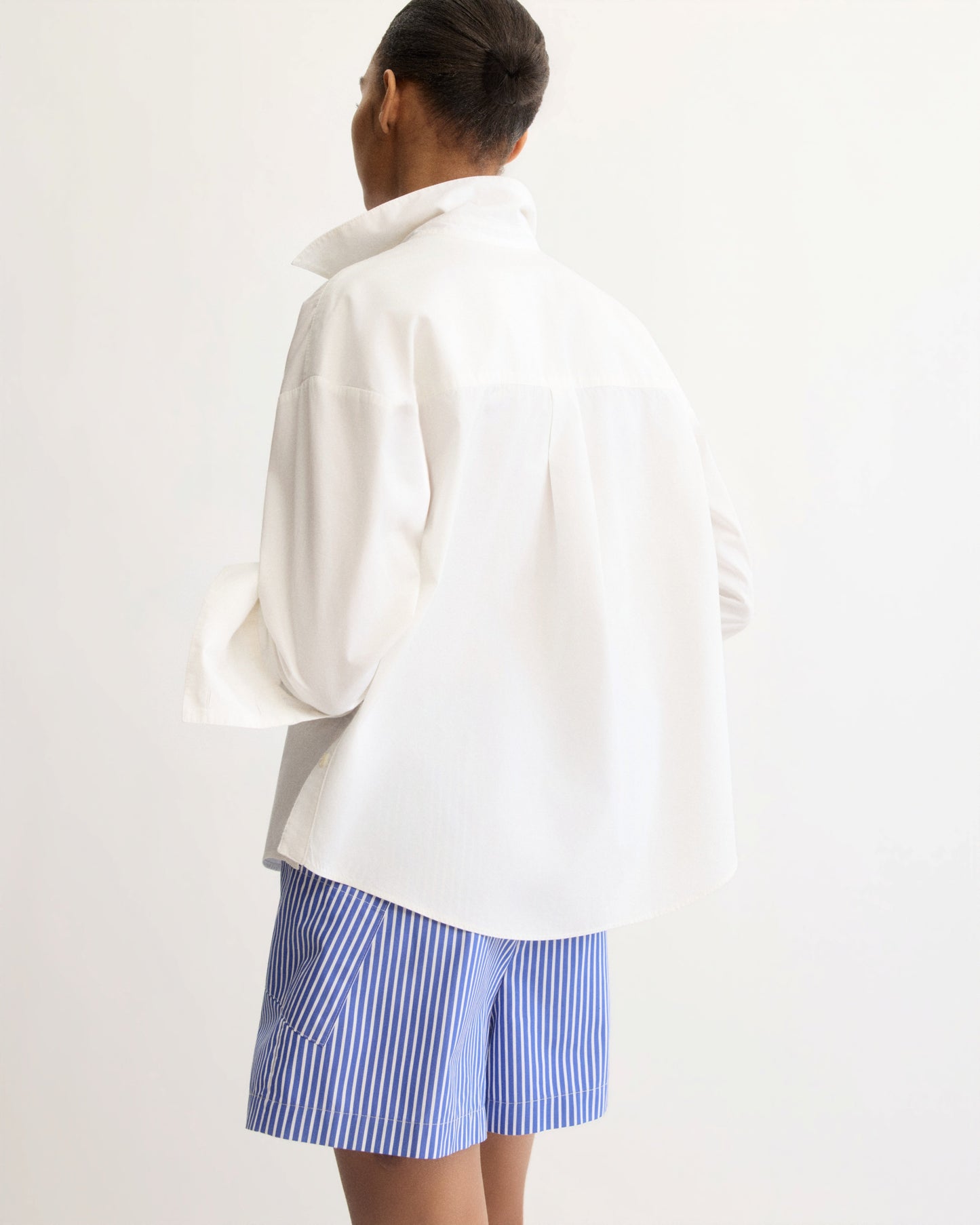 Back view of model wearing white oversized button shirt with blue striped shorts