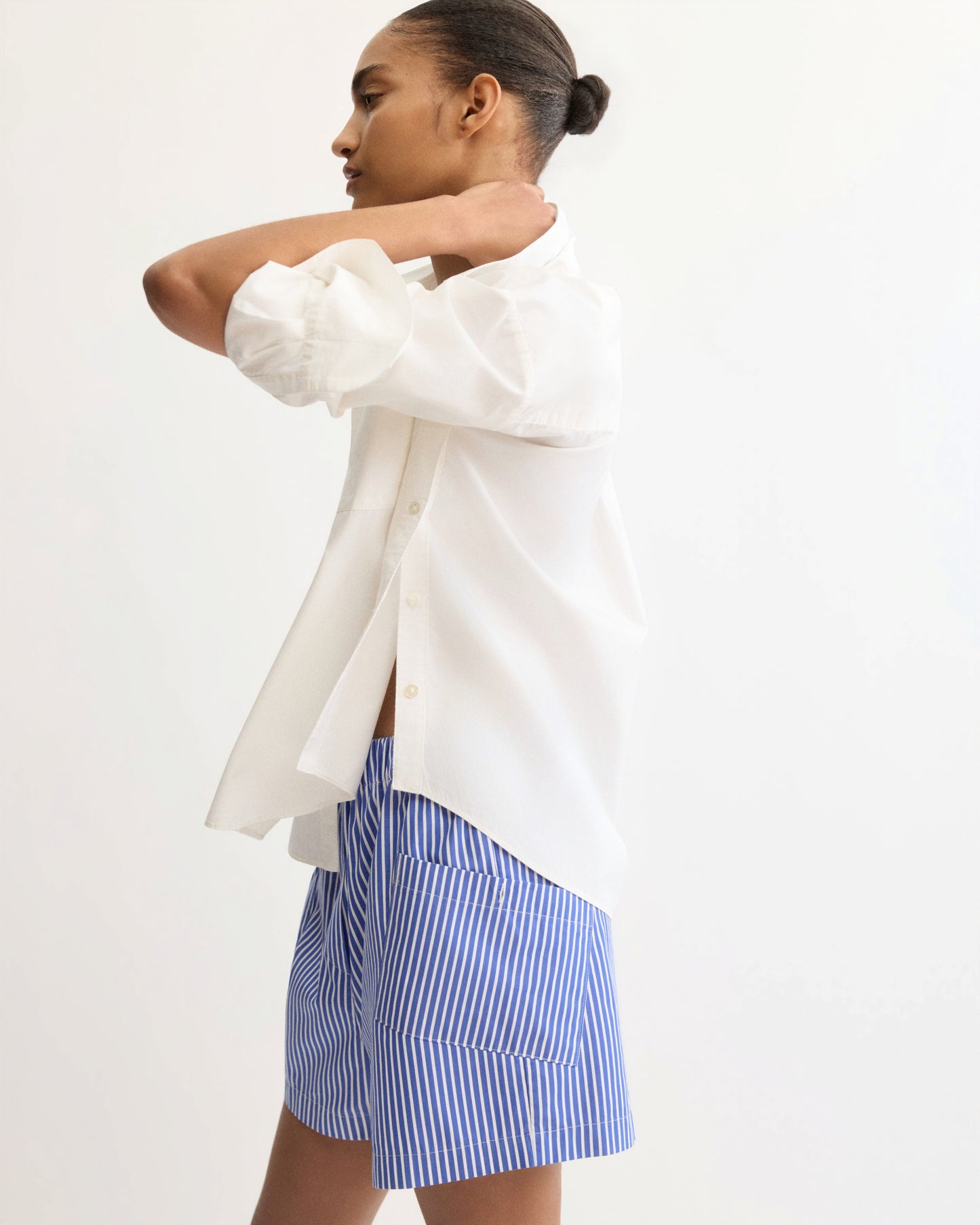 Model wearing white button shirt with side detail, back view on white background
