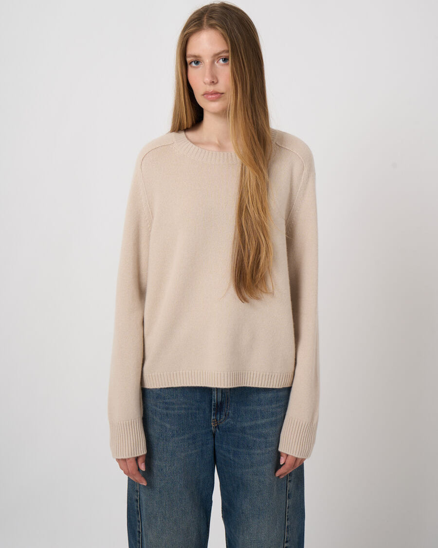 Women's beige cashmere crew neck sweater with ribbed cuffs and hem worn with blue jeans