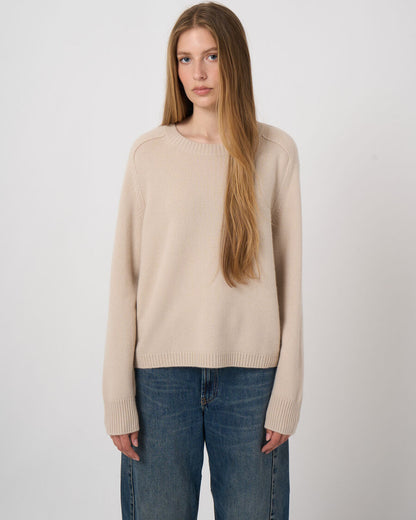 Women's beige cashmere crew neck sweater with ribbed cuffs and hem worn with blue jeans
