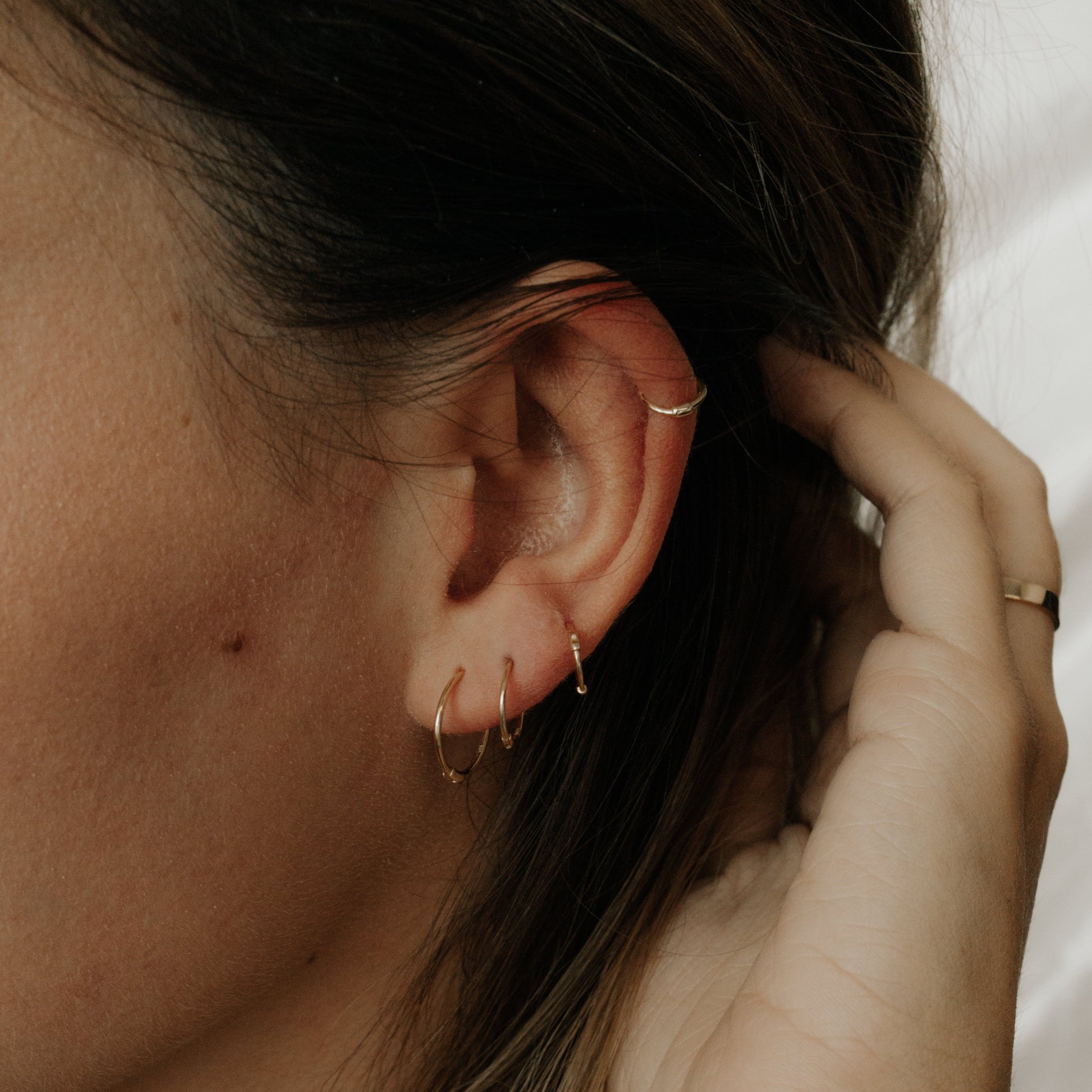 Model wearing small gold thin huggie earrings in multiple ear piercings