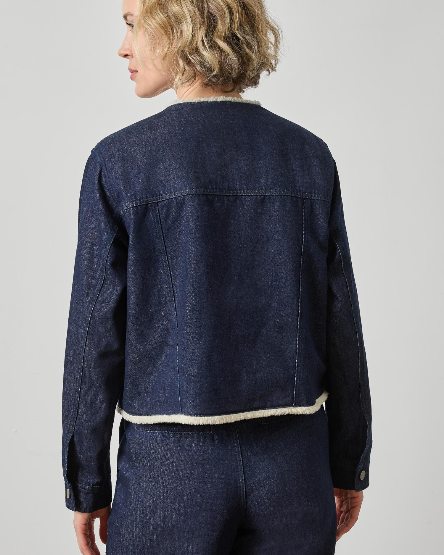 Dark wash blue denim jacket with cream sherpa trim at collar and hem
