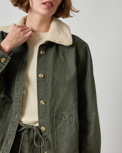 Olive green twill jacket with sherpa collar and gold buttons, layered over cream ribbed sweater