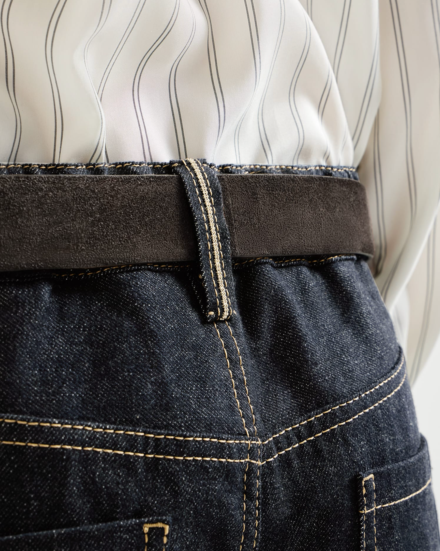Dark indigo denim trousers with gold stitching, monili belt loop, and gray suede belt