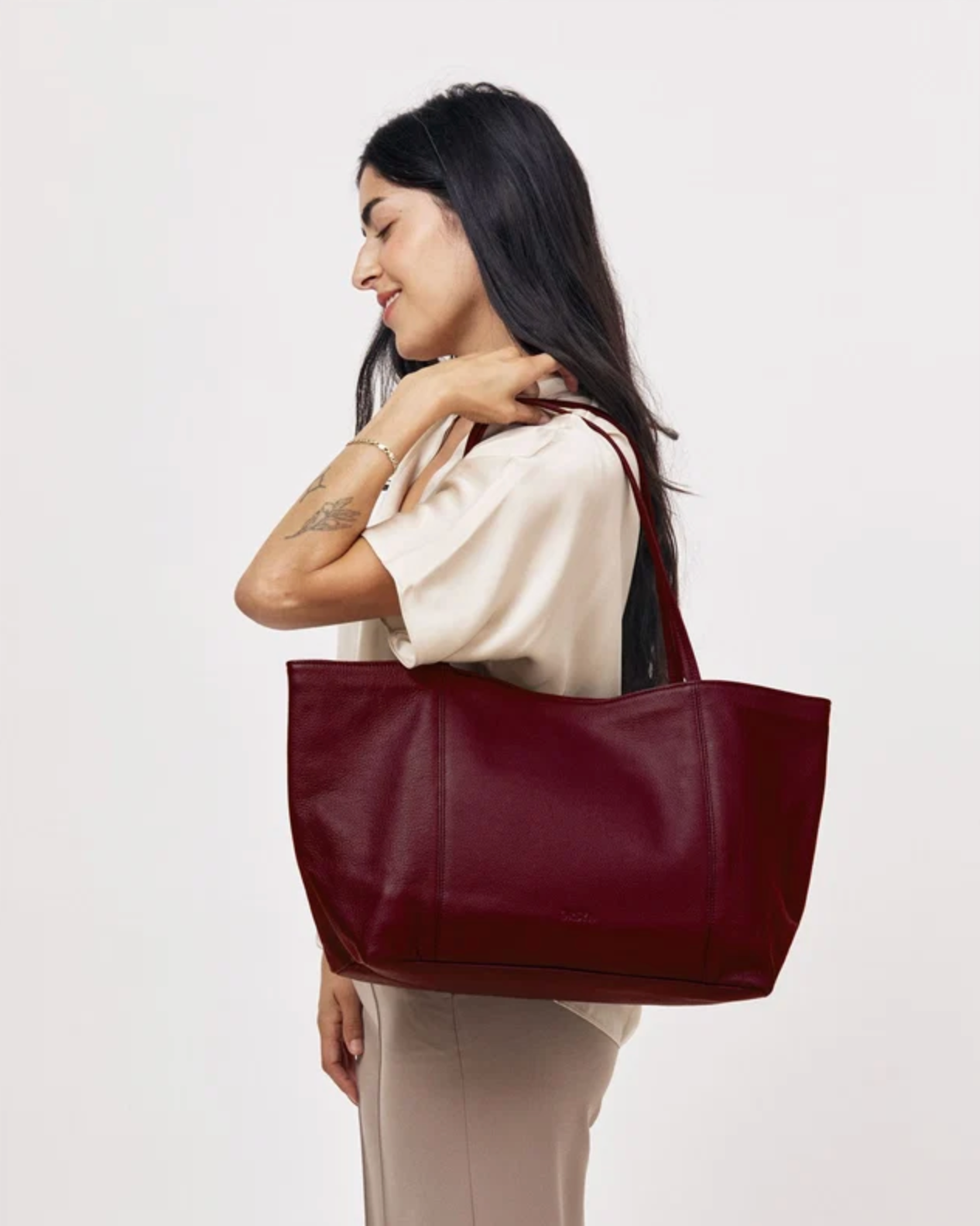 Makena Tote in Plum Pebble Grain leather carried on shoulder by a model