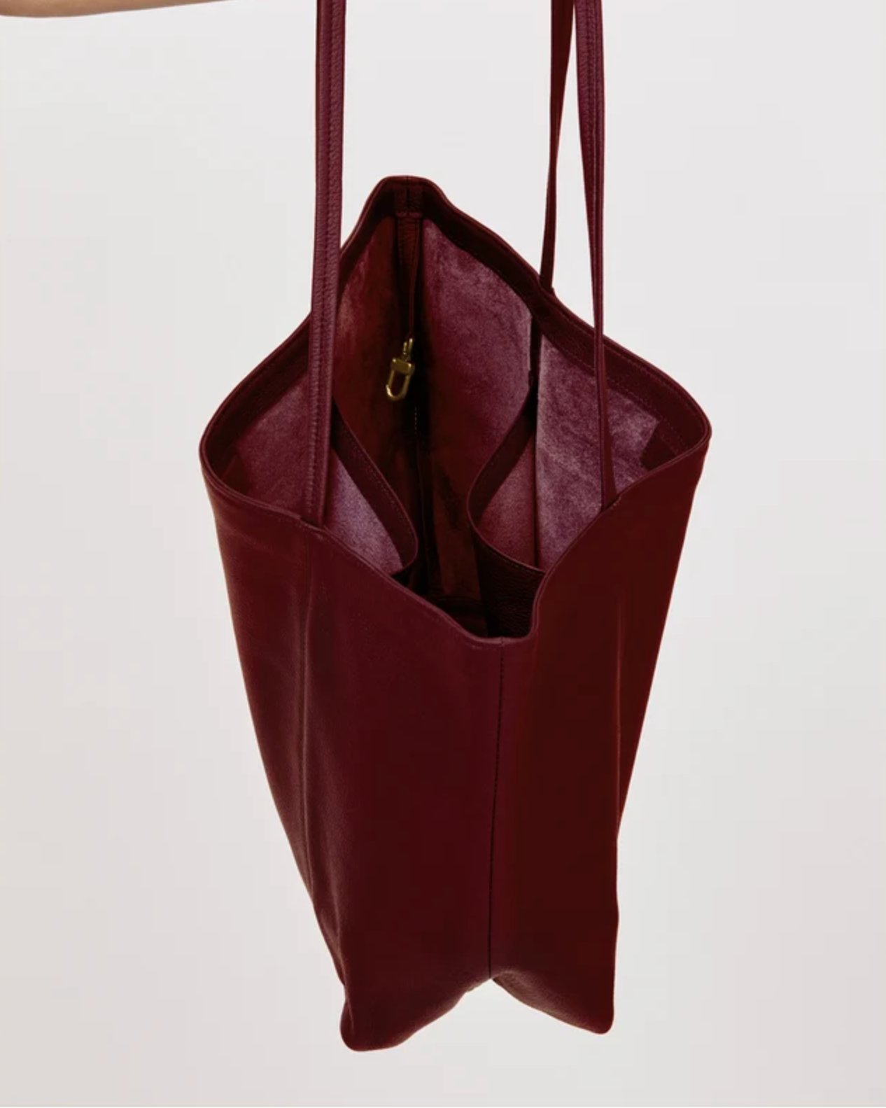 Makena plum leather tote bag shown open, revealing interior pocket with gold zipper pull.