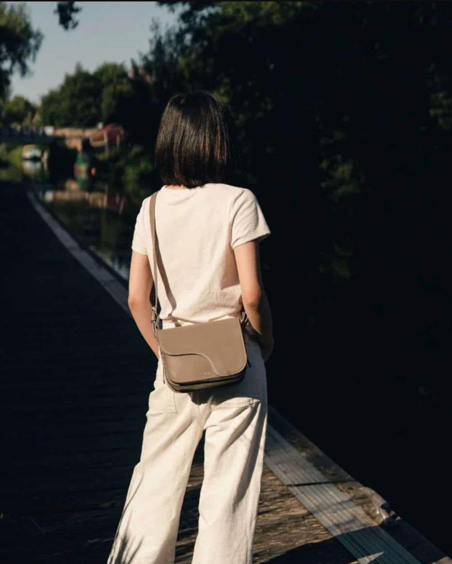 Mud crossbody saddle bag worn over shoulder, cream outfit, canal path setting.