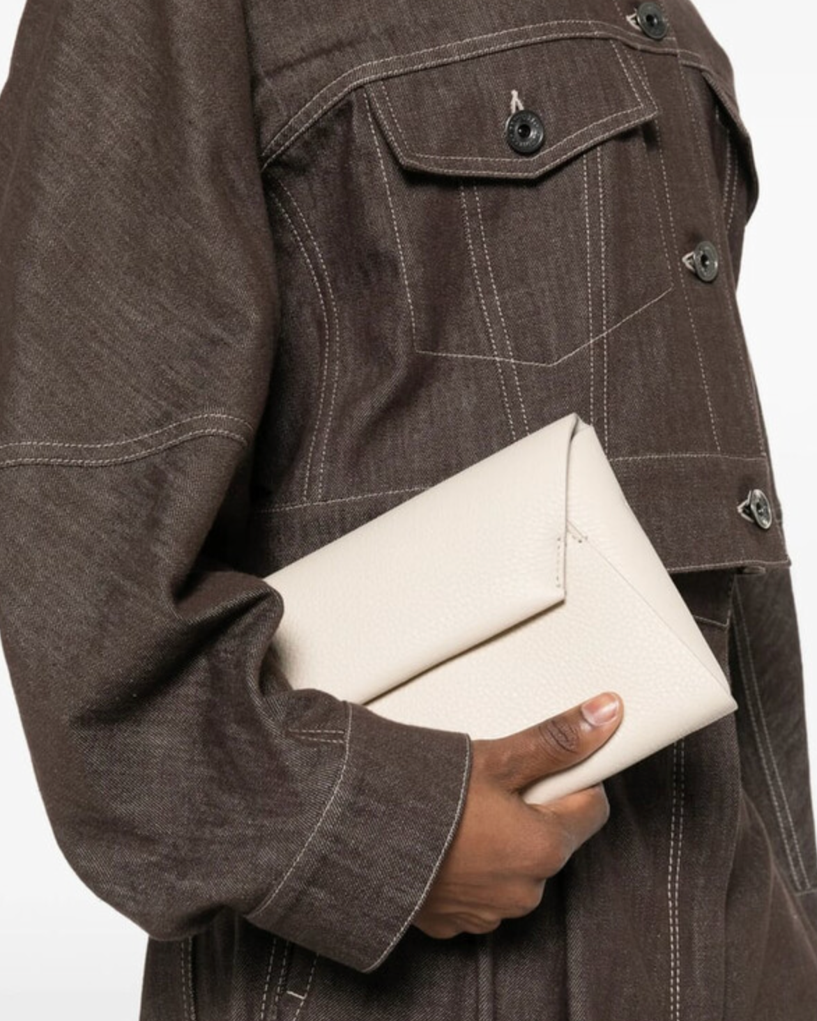 Brunello Cucinelli ivory leather envelope clutch held against brown denim jacket