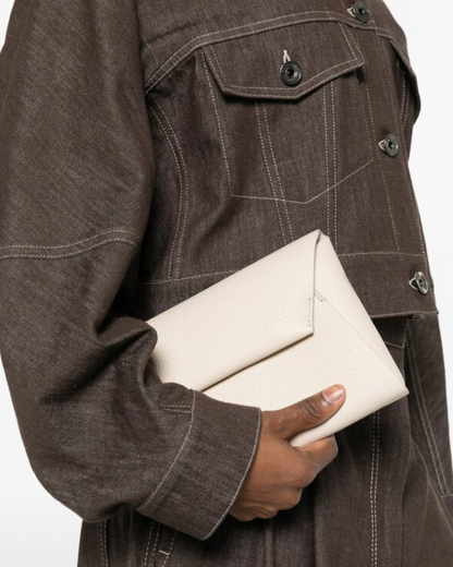 Brunello Cucinelli ivory leather envelope clutch held against brown denim jacket