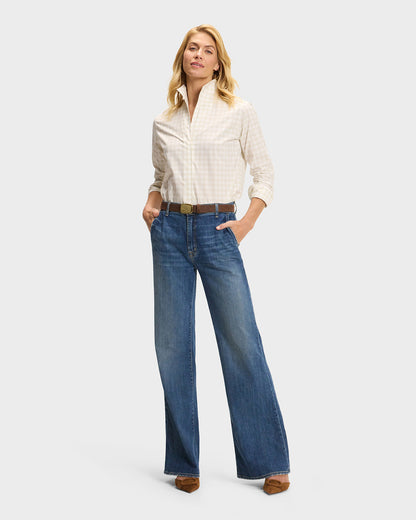 Model wearing cream gingham button-down shirt tucked into wide-leg blue jeans with brown belt