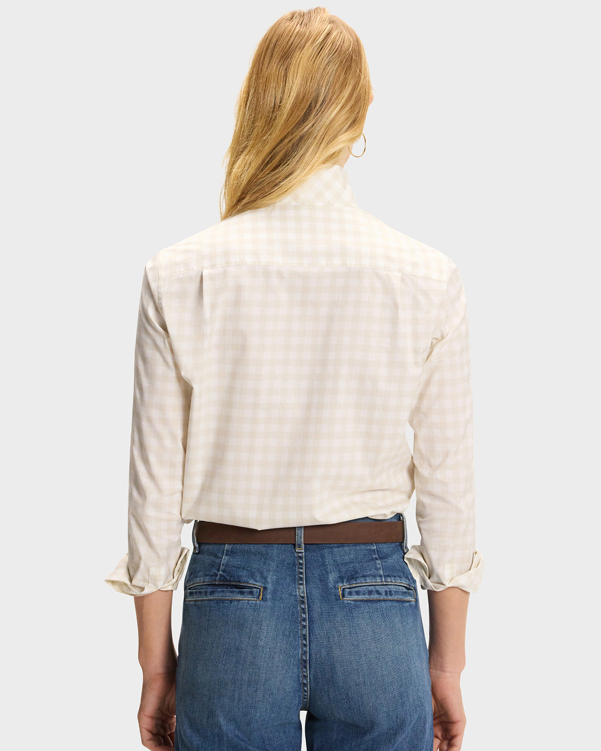 Back view of model wearing cream gingham button-up shirt tucked into blue jeans with brown belt