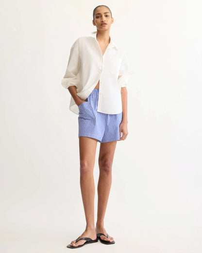 Model wearing white oversized button-up shirt with blue striped shorts and black sandals