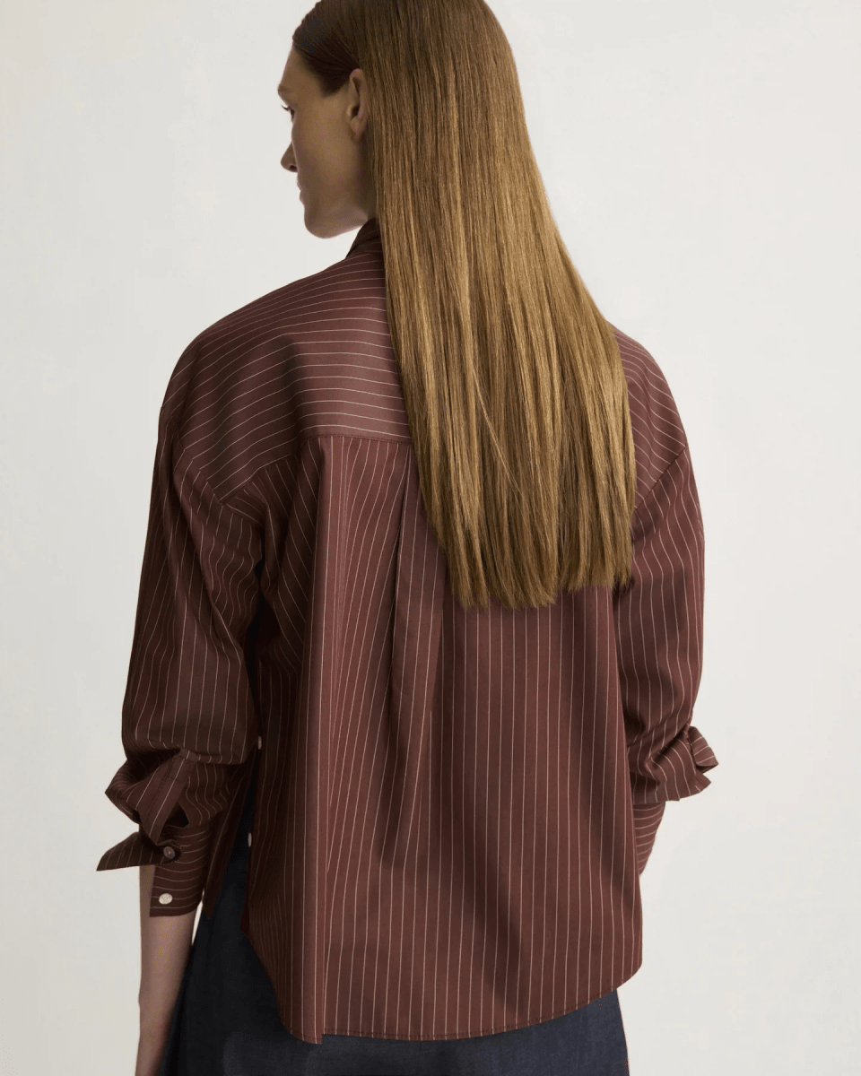 Back view of model wearing oxblood pinstripe oversized button shirt with long sleeves