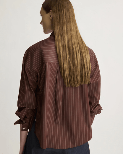 Back view of model wearing oxblood pinstripe oversized button shirt with long sleeves